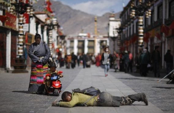 一名孩童看着西藏拉萨大昭寺外面叩头的朝圣者 照片／REUTERS/Jacky Chen/File Photo